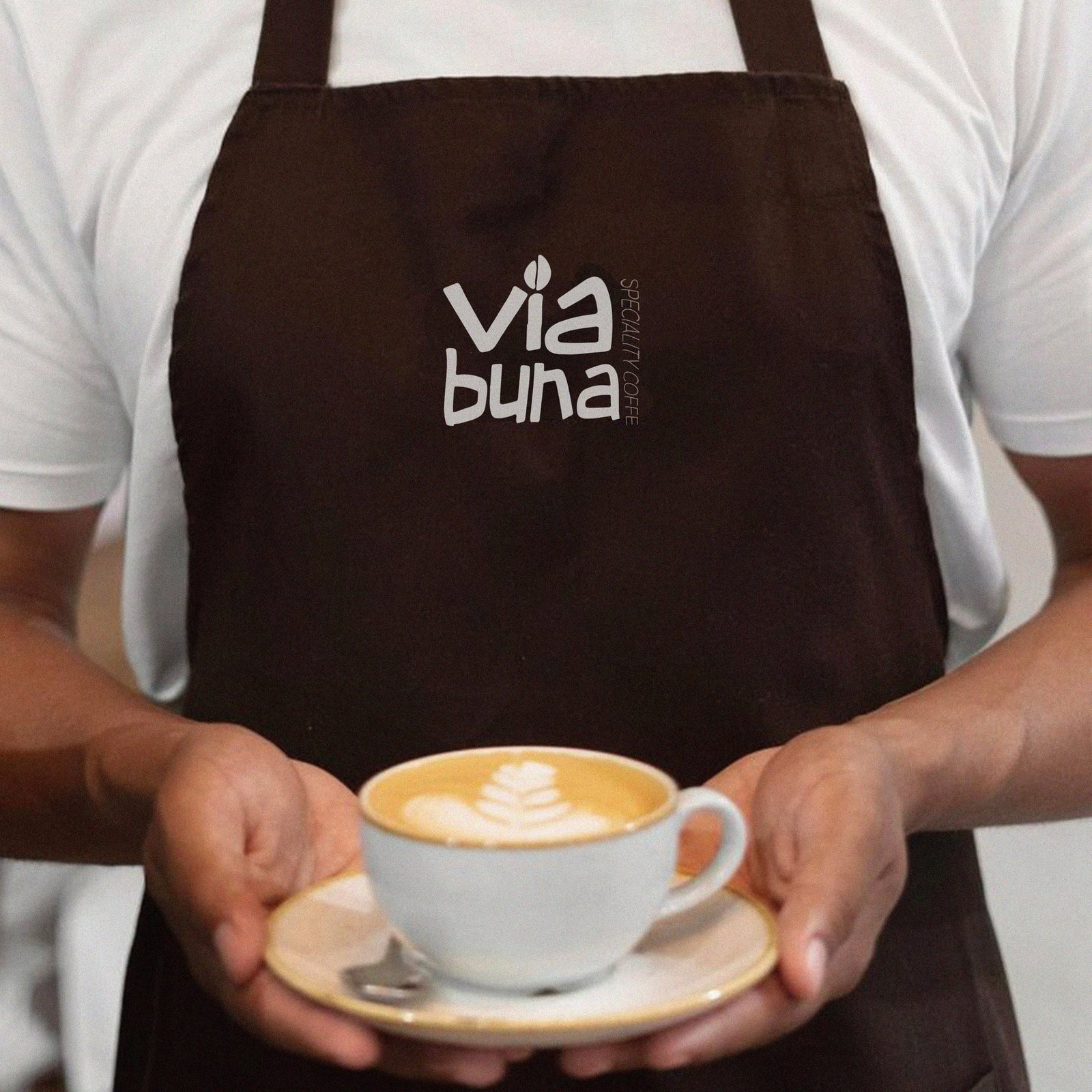Barista in a Via Buna apron pouring latte art